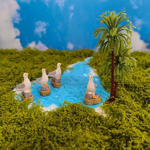 Peut inclure: Scène miniature avec quatre mouettes grises et blanches perchées sur des poteaux en bois, disposées autour d'une rivière bleue. Un petit palmier est présent, sur fond de mousse verte et de ciel bleu nuageux. Thème côtier ou tropical.
