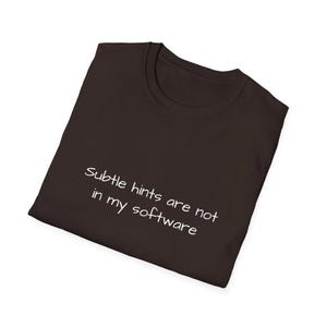 Puede incluir: Una camiseta marrón oscuro con el texto blanco "Subtle hints are not in my software." La camiseta doblada muestra un cuello redondo. El texto está centrado en la parte delantera de la camiseta. Una prenda informal.