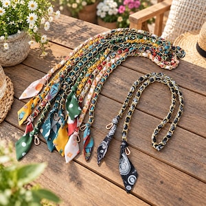 May include: A collection of bag straps featuring gold-tone metal chains interwoven with colourful patterned fabric ribbons. Each strap includes a small metal lobster clasp at both ends, showcasing various prints including polka dots, paisley, and floral motifs.