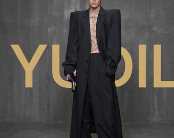Oversized zwarte trenchcoat, lange jas met extreem brede schouders, avant-garde broek met wijde pijpen