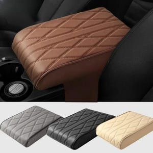 Può includere: Un bracciolo per auto marrone, trapuntato a rombi, è mostrato, installato in un veicolo. Sotto, sono mostrati tre braccioli aggiuntivi in grigio, nero e beige. I braccioli sono realizzati in un materiale simile alla pelle e sono progettati per il comfort e lo stile.