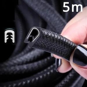 May include: A black rubber edge trim with a textured surface is held in a hand. The trim has a U-shaped channel and a white interior. The image also shows the text "5m".