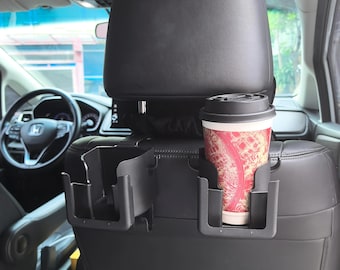 Peut inclure: Organisateur de siège de voiture noir avec deux porte-gobelets et un petit compartiment de rangement. Un gobelet de café jetable avec un motif rouge et blanc est dans l'un des porte-gobelets. L'organisateur se fixe à l'arrière d'un siège de voiture.