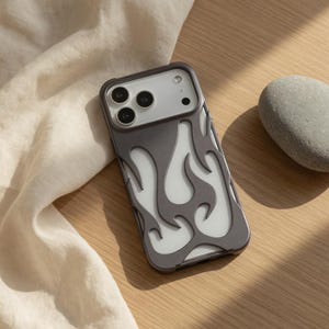 Op de afbeelding: Een grijze telefoonhoes met een vlammenontwerp. De hoes heeft een donkergrijze rand en een witte achtergrond met grijze vlamvormen. De telefoonhoes ligt op een houten oppervlak.