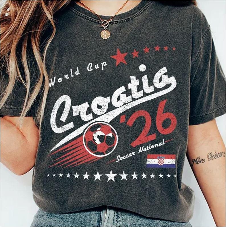 May include: A charcoal gray t-shirt featuring a distressed graphic print that reads World Cup Croatia '26 Soccer National. The design includes a red soccer ball, a row of stars, and the Croatian flag in red, white, and blue colors.