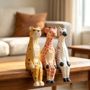 Peut inclure: Trois figurines d'animaux en bois sculptées à la main assises sur un rebord. L'ensemble comprend un léopard jaune à taches brunes, une girafe orange rosé à motif quadrillé et un zèbre blanc à rayures noires, avec des marques de ciseau visibles.