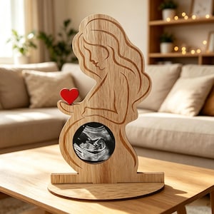 May include: A light-colored wooden cutout sculpture depicting a pregnant figure in profile. The figure features engraved lines representing hair and body contours, with a circular cutout at the abdomen containing a black and white ultrasound image.