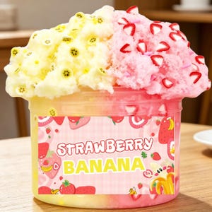 May include: A clear plastic container filled with colorful slime. The slime is divided into yellow and pink sections, decorated with fruit-shaped sprinkles. The label reads "STRAWBERRY BANANA" with fruit illustrations.