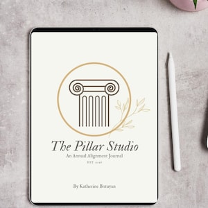 May include: A digital tablet displays the cover of "The Pillar Studio" annual alignment journal. The cover features a gold-colored pillar design within a circle, with text below. A white stylus rests beside the tablet.