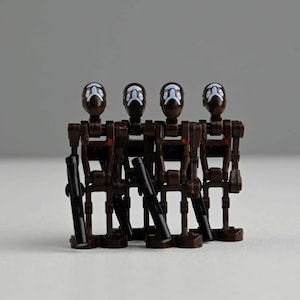 May include: Four brown and black toy figures with white facial details and black weapons. The figures are standing upright, with a minimalist design. The background is a plain, light gray.