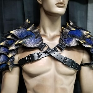 May include: Blue and gold dragon scale shoulder armour with black leather straps and buckles. The armour is displayed on a mannequin, showcasing the intricate design of the fantasy-themed piece.