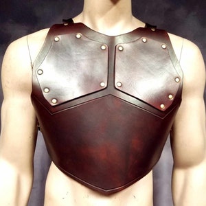 May include: A brown leather chest piece with brass accents. The chest piece is made of multiple leather panels that are stitched together.