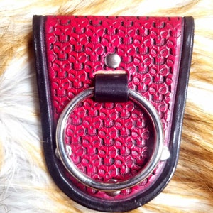 May include: A red leather pouch with a skull pattern, a black border, and a silver ring. The pouch is secured with a metal rivet. The background is a furry texture.