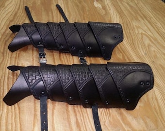 May include: A pair of black leather arm guards with straps and buckles. The guards are made of multiple overlapping pieces of leather, each with a textured surface.