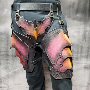May include: A pair of black leather thigh armour with a red and orange gradient paint design. The armour is secured with straps and buckles.