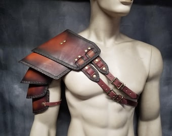 Puede incluir: Una armadura de hombro de cuero marrón con correas y hebillas. La armadura está hecha de múltiples capas de cuero y tiene un aspecto desgastado.