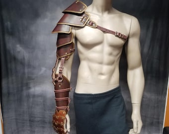 May include: A brown leather arm guard with metal accents and straps. The guard covers the entire arm, from the shoulder to the hand. It has a decorative design with multiple layers of leather and metal.