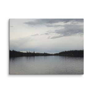 Puede incluir: Impresión en lienzo de una serena escena lacustre bajo un cielo nublado. El agua refleja el cielo y las oscuras siluetas de los árboles que bordean la orilla lejana. La paleta de colores es apagada, con tonos grises y verdes.