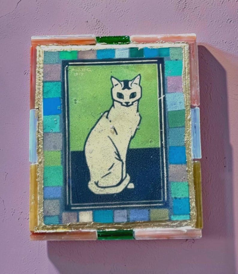May include: A rectangular mosaic wall art piece featuring a central illustration of a seated cat in cream against a green and dark blue background. The artwork is framed by a border of small, multicolored glass tiles in blue, green, and grey.