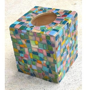 May include: A square tissue box cover featuring a mosaic design made of small, multi-colored glass tiles in shades of blue, green, pink, yellow, and orange. The top surface has a circular opening, and the sides are fully covered in glass pieces.