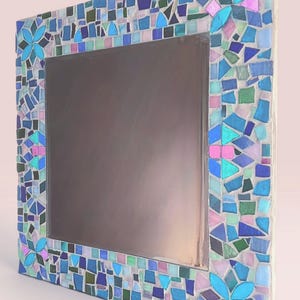 Puede incluir: Un espejo cuadrado con un marco de mosaico decorativo compuesto por peque&ntilde;as piezas de vidrio de formas irregulares en tonos azul, turquesa, verde y rosa claro. El marco incluye cuatro patrones florales distintos en las esquinas.