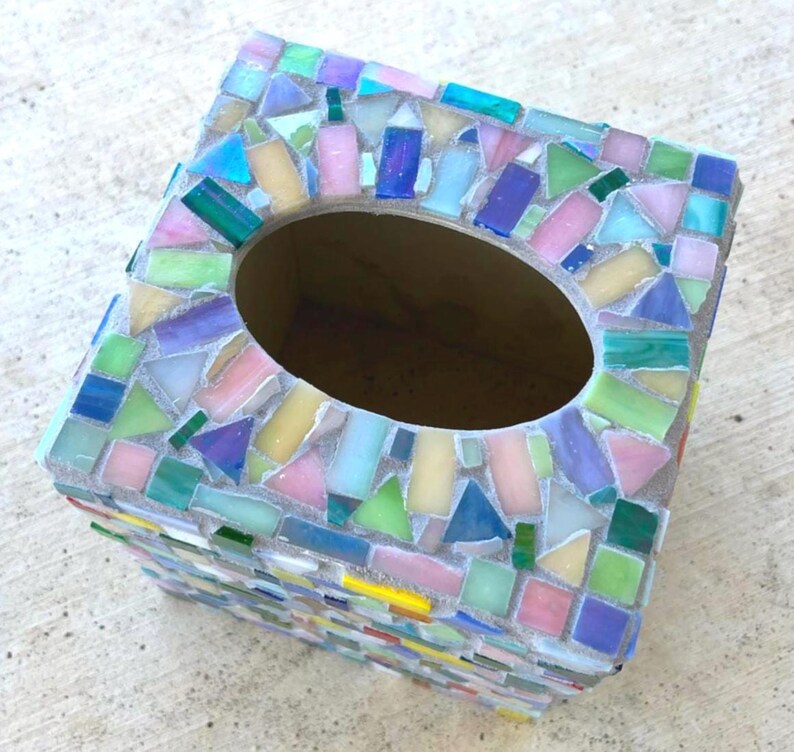 May include: A rectangular tissue box cover featuring a mosaic design made of small, multi-colored glass tiles in shades of pink, blue, green, yellow, and purple. The tiles are arranged in a random pattern and set in light gray grout.