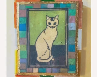May include: A rectangular wall art piece featuring a central illustration of a seated cream-colored cat against a green and dark blue background. The artwork is framed by a border of small, multicolored glass tiles in shades of blue, green, and orange.