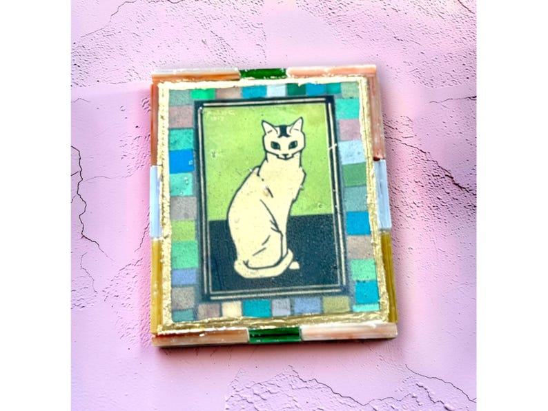 May include: A rectangular wall art piece featuring a central illustration of a seated cream-colored cat against a lime green and black background. The image is framed by a mosaic border of small, multi-colored glass tiles and gold leaf accents.