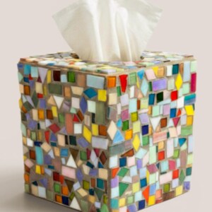 May include: A square tissue box cover decorated with a multi-colored mosaic pattern of small glass tiles in shades of red, blue, yellow, green, and purple, set in gray grout, with a white tissue protruding from the top opening of the container.