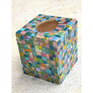 May include: A square tissue box covered in colorful mosaic tiles. The mosaic features a variety of colors, including blue, green, pink, yellow, and orange. The top has a circular opening for tissue dispensing.