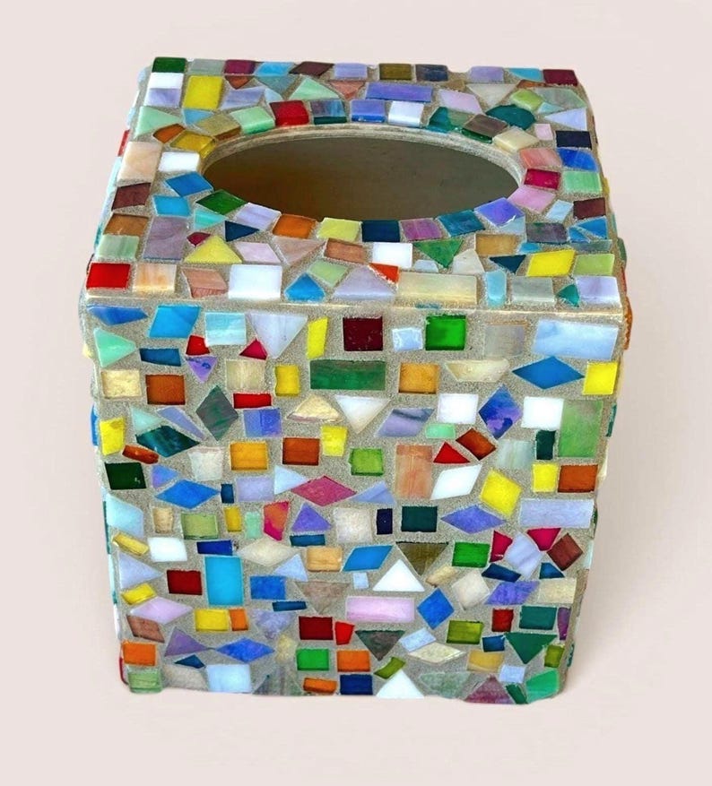 May include: A square tissue box cover decorated with a mosaic of multicolored glass tiles in shades of red, blue, green, yellow, and white. The tiles are arranged in various geometric shapes and set into a light gray grout, featuring an oval opening.