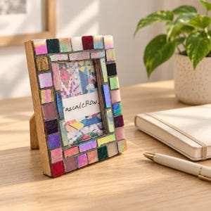 May include: A rectangular picture frame with a wooden base decorated with a mosaic of small, multicolored tiles in shades of pink, red, blue, green, and iridescent white. The center displays a white card with the text "pascaleRow" in black.