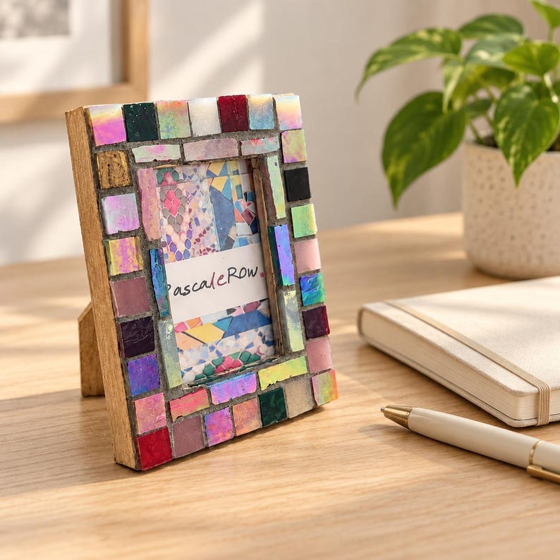 May include: A rectangular picture frame with a wooden base decorated with a mosaic of small, multicolored tiles in shades of pink, red, blue, green, and iridescent white. The center displays a white card with the text "pascaleRow" in black.