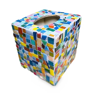 May include: A square tissue box cover decorated with a multi-colored mosaic pattern. The surface features small, irregularly shaped glass tiles in shades of blue, green, yellow, orange, red, and white, set into a white grout base.