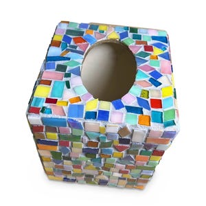 May include: A square tissue box cover decorated with a multi-colored mosaic pattern of small, irregular glass tiles in shades of blue, yellow, red, pink, green, and orange, featuring a central oval opening on the top surface for dispensing tissues.