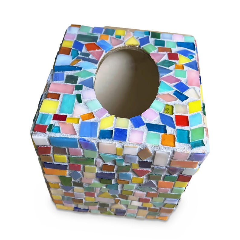 May include: A square tissue box cover decorated with a multi-colored mosaic pattern of small, irregular glass tiles in shades of blue, yellow, red, pink, green, and orange, featuring a central oval opening on the top surface for dispensing tissues.