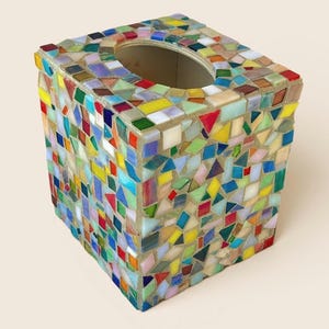 May include: A square tissue box cover featuring a mosaic design made of small, multi-colored glass tiles in shades of red, blue, yellow, green, and white. The tiles are arranged in a random pattern and set into a light-colored grout base.