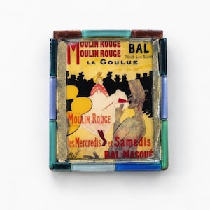 May include: A rectangular decorative tile featuring a Moulin Rouge La Goulue poster print, framed by a border of small, multi-colored glass tiles in shades of blue, green, and brown, with gold-toned metal accents surrounding the central image.