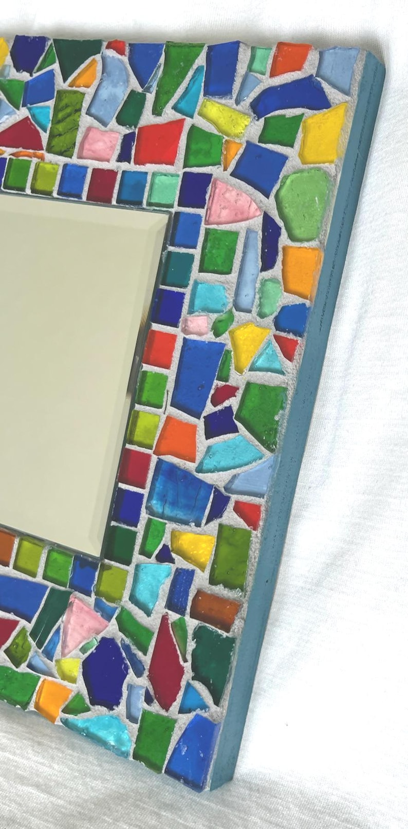 May include: A rectangular wall mirror featuring a mosaic frame constructed from numerous small, irregularly shaped pieces of translucent glass in vibrant shades of red, orange, yellow, green, and blue, all set within a light gray grout border.