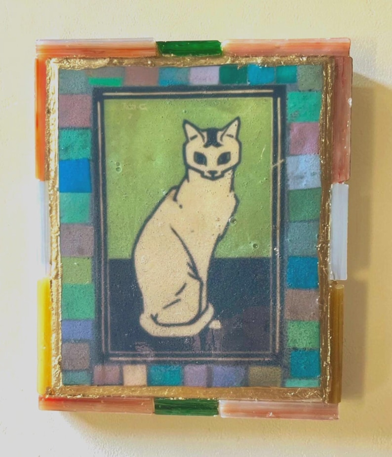 May include: A rectangular wall art piece featuring a central illustration of a seated cat against a green and dark blue background. The image is framed by a border of small, multi-colored glass tiles in shades of blue, green, and pink, with a gold-toned trim.