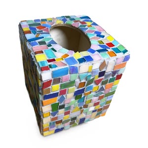 May include: A square tissue box cover decorated with a multi-colored mosaic pattern. The surface features small, irregularly shaped glass tiles in shades of blue, yellow, pink, orange, green, and white, all set within white grout.
