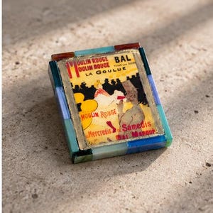 May include: A rectangular decorative box featuring a Moulin Rouge La Goulue poster print on the lid. The frame is constructed from small, multi-colored rectangular tiles in shades of blue, green, and amber, surrounding a central image.