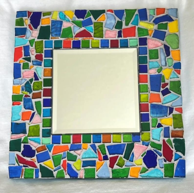May include: A square mirror featuring a decorative frame composed of multi-colored glass mosaic tiles. The frame displays an array of irregular and square-shaped pieces in shades of blue, green, yellow, orange, red, and pink, set in white grout.