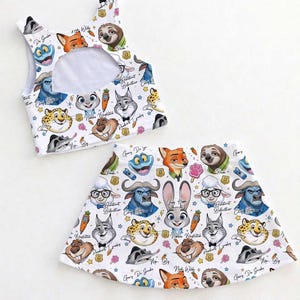 May include: A white two-piece outfit featuring cartoon characters from Zootopia. The top is a crop top with a cutout, and the skirt is a flared mini skirt. The print includes characters like Judy Hopps, Nick Wilde, and Flash.