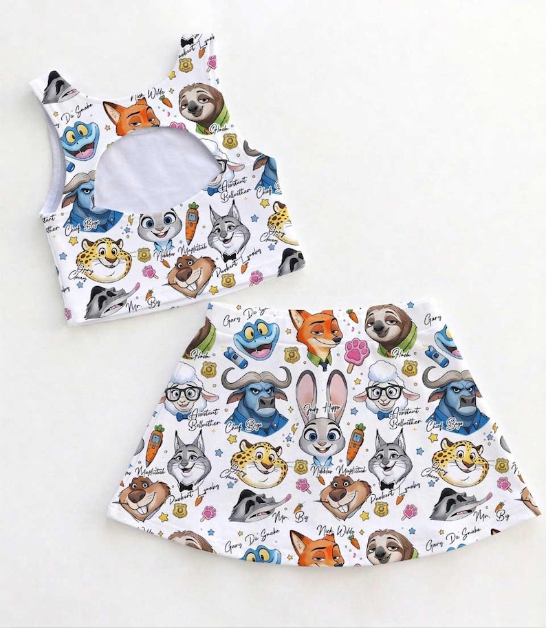 May include: A white two-piece outfit featuring cartoon characters from Zootopia. The top is a crop top with a cutout, and the skirt is a flared mini skirt. The print includes characters like Judy Hopps, Nick Wilde, and Flash.