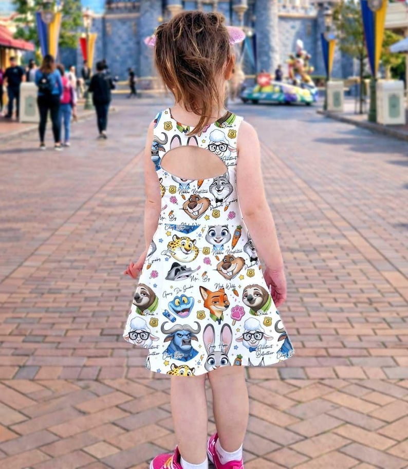 May include: A white sleeveless dress featuring cartoon characters from the movie Zootopia. The dress has a keyhole back and a flared skirt. The characters include Judy Hopps, Nick Wilde, and Flash. The dress is worn by a young child.