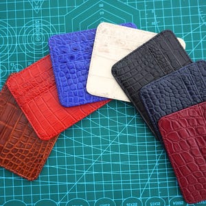 Peut inclure: Un ensemble de sept porte-cartes rectangulaires disposés en éventail. Les porte-cartes présentent un motif texturé en peau de crocodile et sont disponibles en plusieurs couleurs, dont marron, rouge, bleu, crème, noir, bleu foncé et bordeaux.