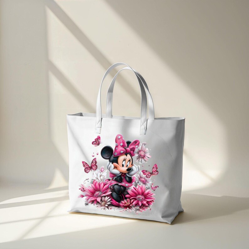 May include: White tote bag featuring a Minnie Mouse graphic. Minnie is wearing a pink dress and bow, surrounded by pink flowers and butterflies. The bag has two white handles and is made of a sturdy material.