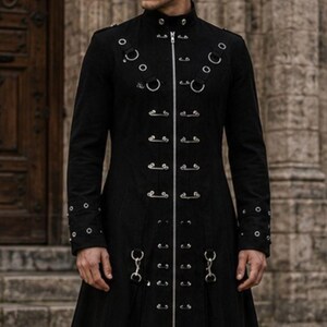 May include: A long black coat with a high collar and silver metal detailing. The coat has a series of rings and clasps down the front and on the sleeves. The coat has a flared skirt and is made of a heavy fabric.