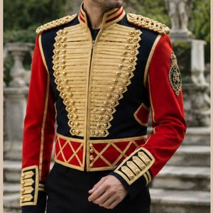 May include: A navy blue and red military-style jacket featuring gold braided cord detailing, gold-tone buttons, and gold epaulets on the shoulders. The front displays a structured design with horizontal gold trim and a red lattice pattern at the waist.